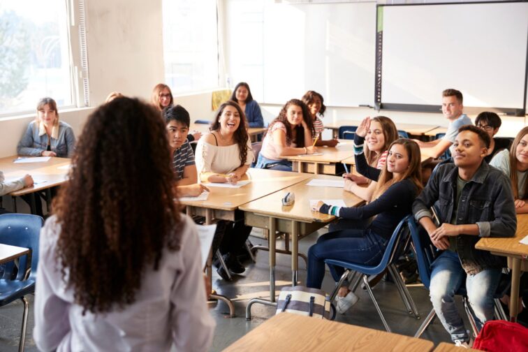 Teacher leading a lively high school class discussion while students lean in and raise hands