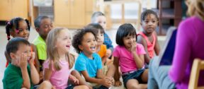 Preschoolers laughing on the rug during morning circle with their teacher